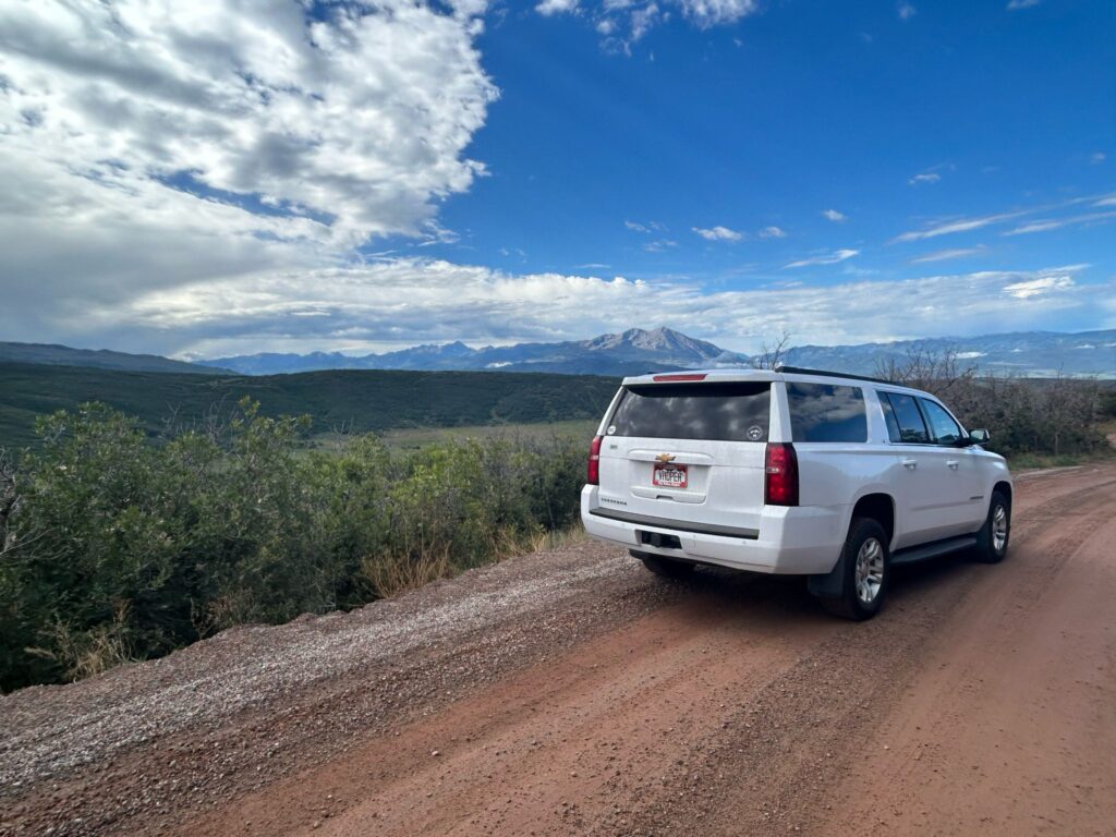 White vehicle waiting roadside beside muddy road.